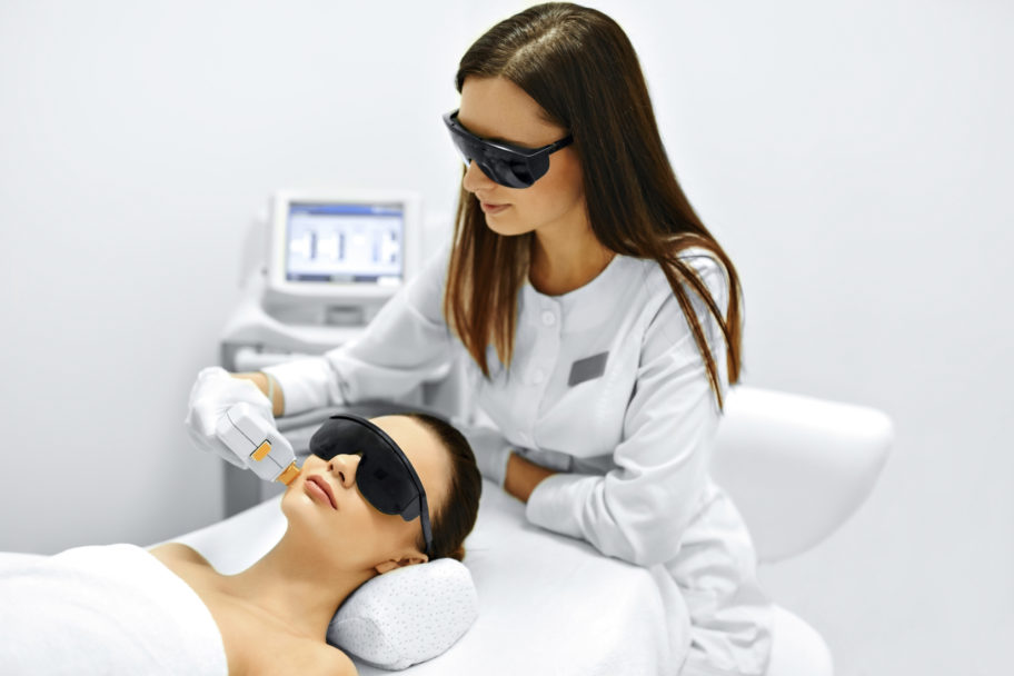 technician performing laser therapy to the face of a relaxed female patient, both wearing protective eyewear